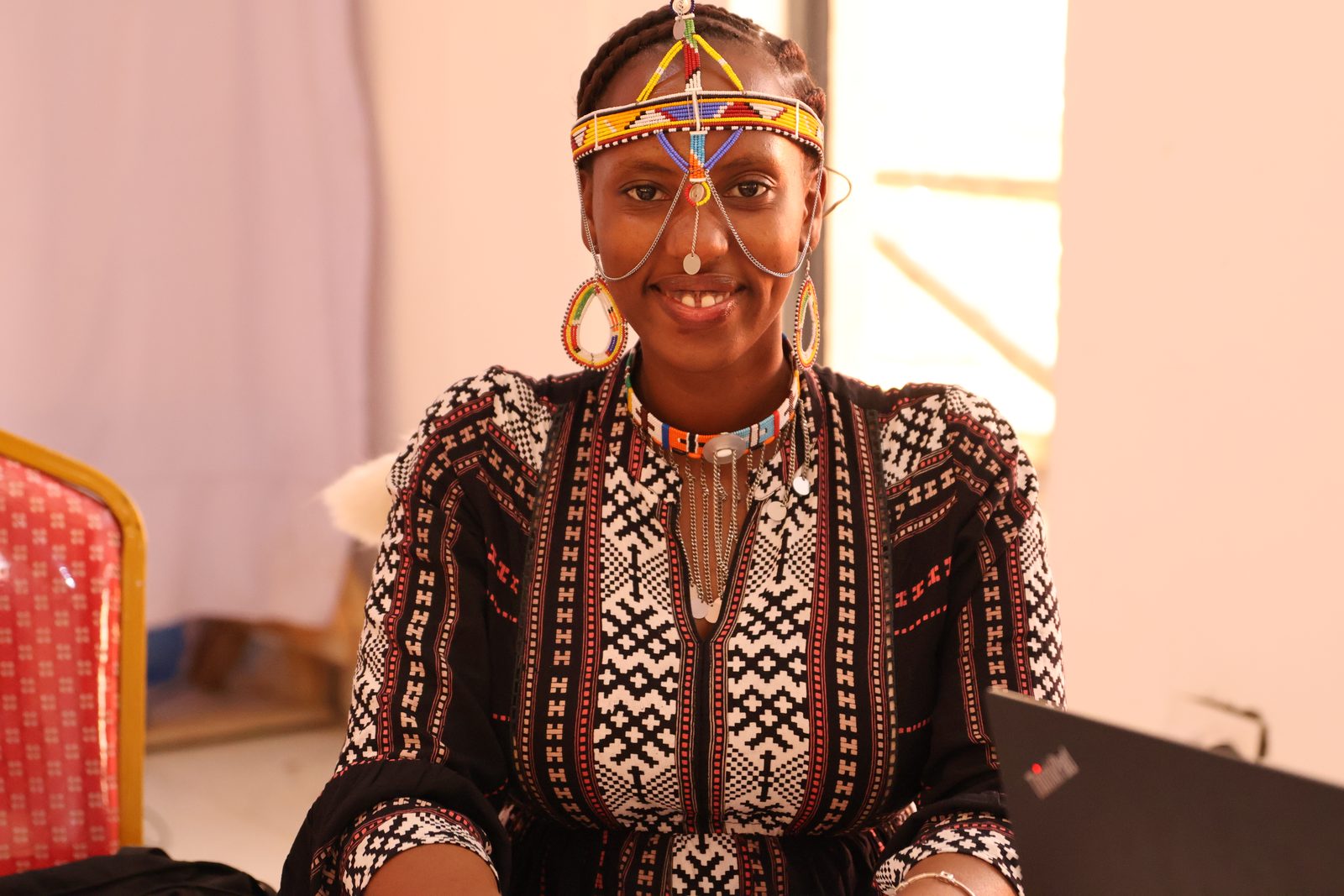 A woman in traditional Maasai beaded jewellery and headpiece smiles at the camera during a session.