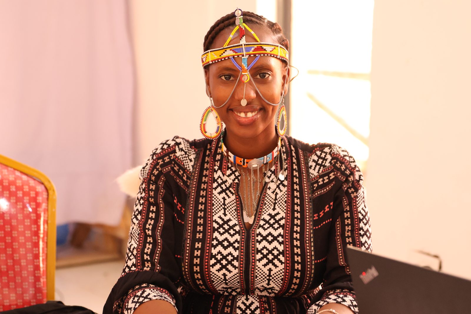 A portrait of a smiling participant wearing an ornate beaded Maasai headband and earrings.