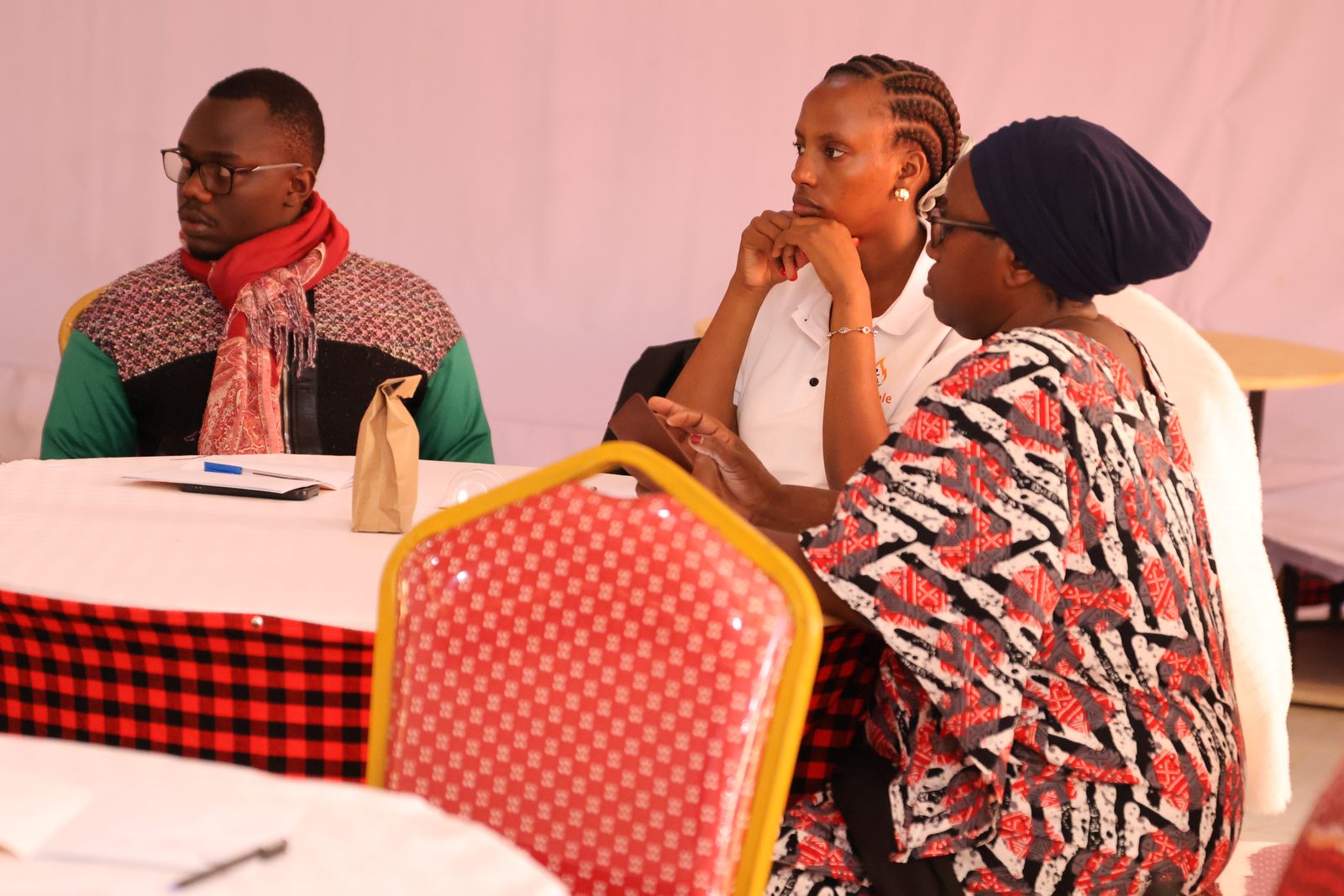 Three participants listen intently during a session, seated around workshop tables.