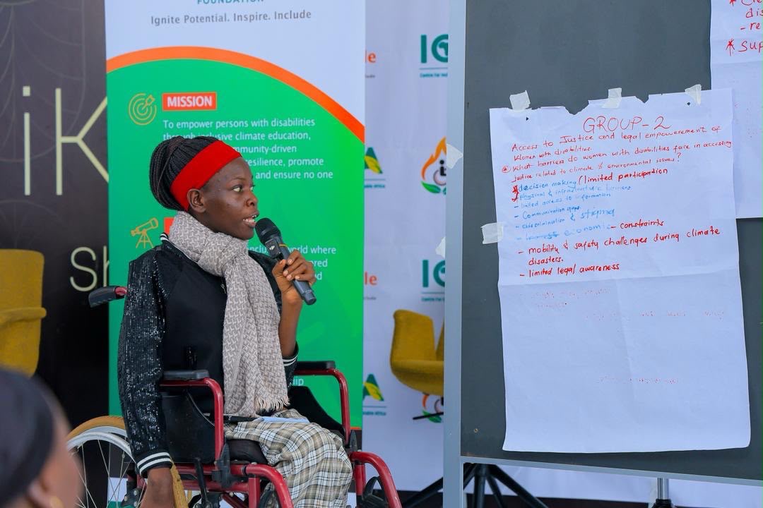 A young woman using a wheelchair speaks into a microphone during a group feedback session.